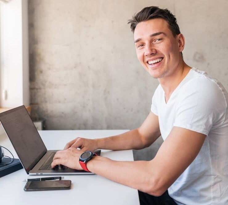 young-handsome-smiling-man-casual-outfit-sitting-table-working-laptop_285396-9078 (1) (1)